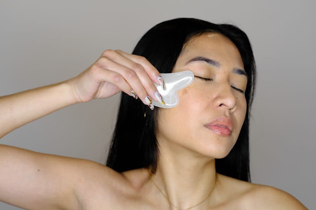 Mujer utilizando una herramienta de gua sha en su mejilla para masaje facial.