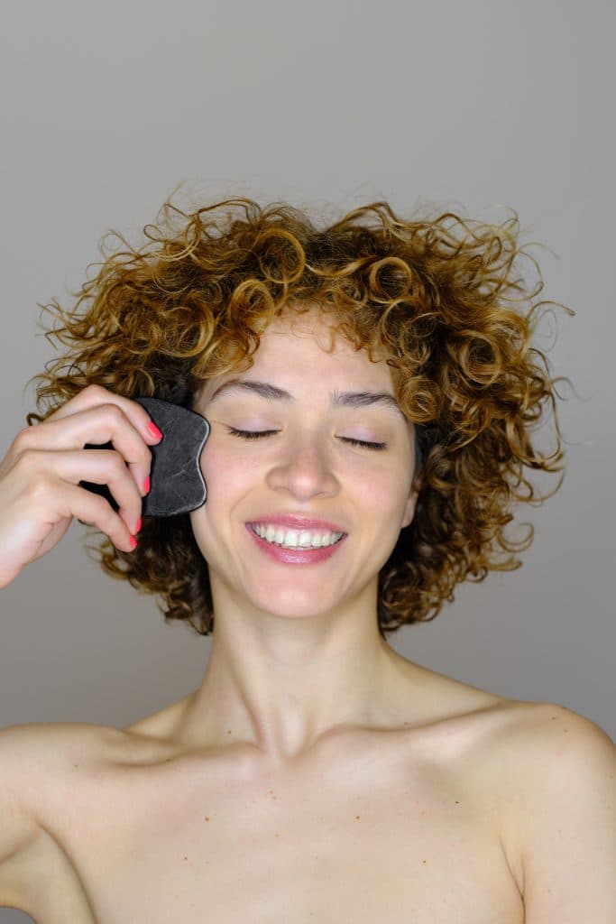 Mujer sonriente aplicando una máscara de ojos de piedra negra sobre su rostro.