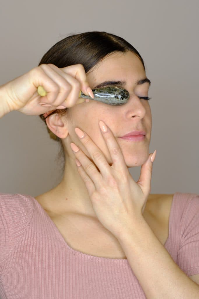 Mujer aplicando un rodillo facial de jade alrededor del área de los ojos.