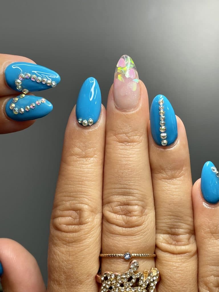 Mano con uñas largas pintadas en tonos de azul y decoradas con perlas y gemas.