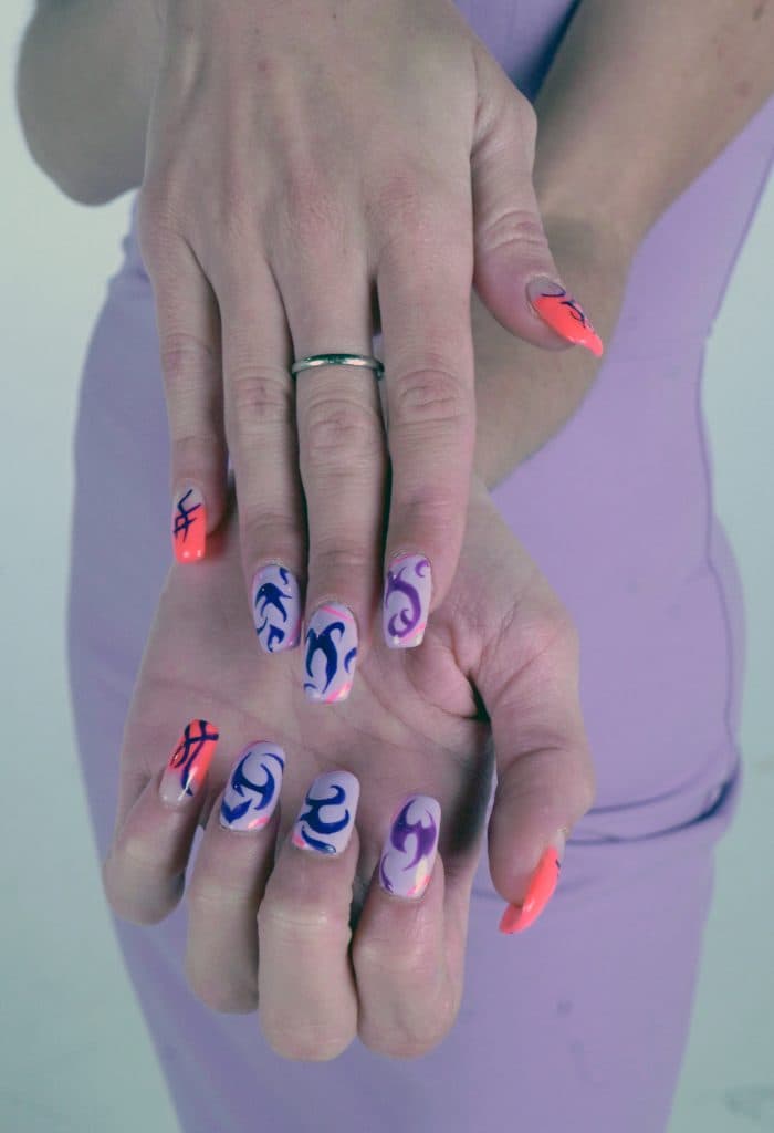 Mano con uñas largas decoradas con diseños abstractos y colores neón sobre una base transparente.