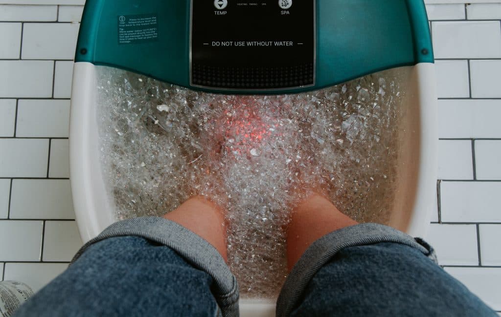 Pies sumergidos en un baño de hidromasaje para pies, con burbujas de agua alrededor.